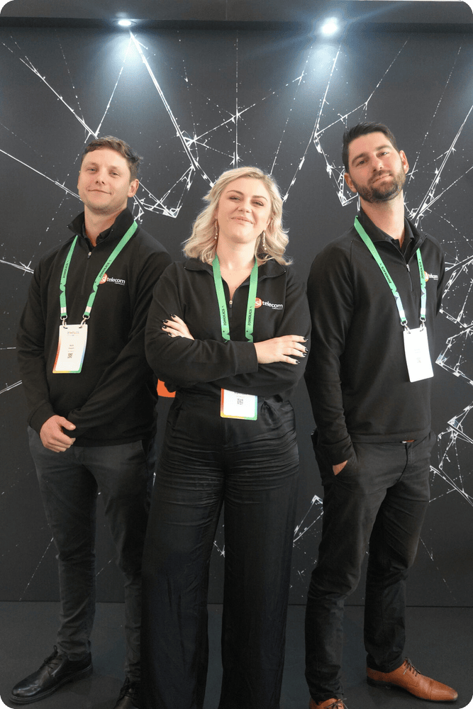 Three DSL Telecom team members at the Break the Glass stand backdrop at Zoholics 2026