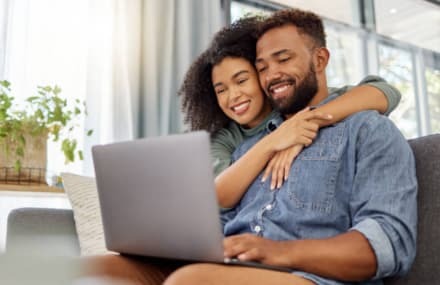Happy couple browsing a laptop at home with reliable Vox Frogfoot fibre internet